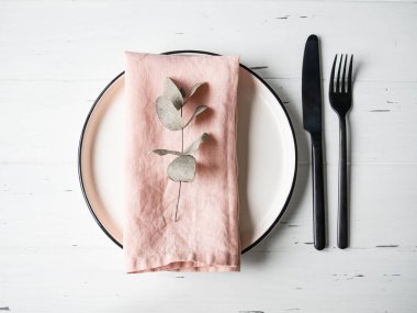 Tabaklı, pembe peçeteli, okaliptüslü ve beyaz ahşap masadaki aletli kırsal masa. Üst görünüm.