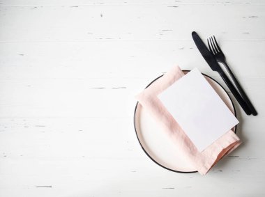 Tabak, pembe peçete, kart ve beyaz ahşap masada bulunan kırsal masa seti. Üst görünüm.