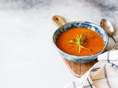Baharatlı taze domates çorbası ve açık arkaplandaki ahşap tahtada mavi bir kabın içinde taze bezelye filizi. Boşluğu kopyala