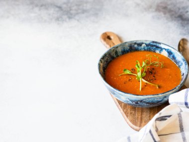 Baharatlı taze domates çorbası ve açık arkaplandaki ahşap tahtada mavi bir kabın içinde taze bezelye filizi. Boşluğu kopyala