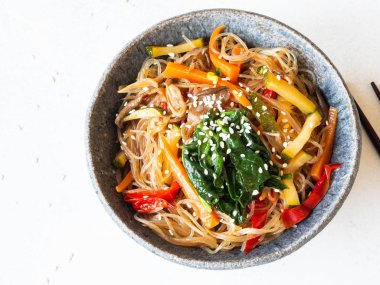 Pirinç erişteli mavi kase ve gri arka planda çeşitli sebzeli sığır kızartması. Üst görünüm