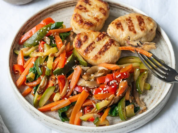 Turkey cutlets grill, vegetables steer fry and white sesame on a plate on the table.