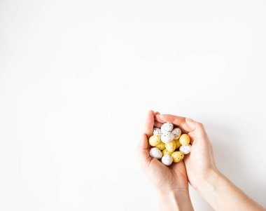 Beyaz arka planda bir avuç dolusu Paskalya sarısı ve beyaz yumurta tutan kadın elleri. Üst Manzara. Boşluğu kopyala