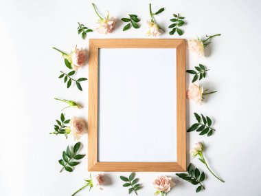 Ahşap çerçeve ve beyaz arka planda yeşil yapraklar ve güllerin yaratıcı bileşimi. Üst görünüm