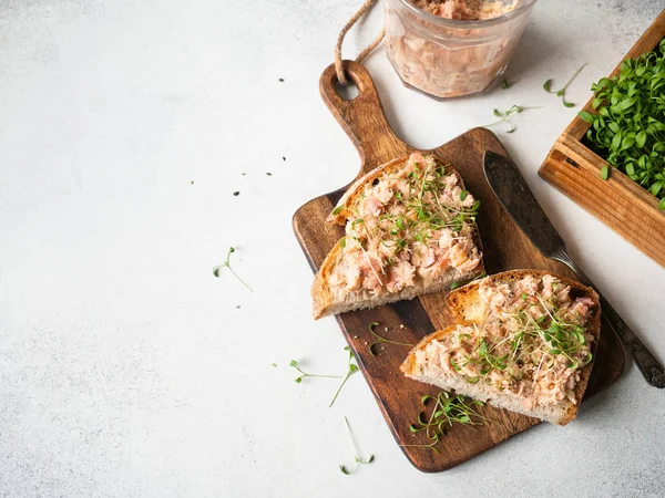 Здорові тости з лососем та свіжими зеленими паростками на дріжджовому хлібі на дошці для різання деревини на сірому фоні. Копіювати простір — стокове фото