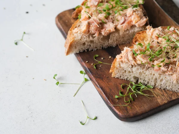 Здорові тости з лососем та свіжими зеленими паростками на хлібі без дріжджів на дошці для різання деревини на сірому фоні . — стокове фото