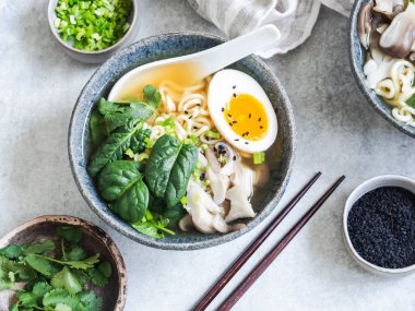 Mantarlı vejetaryen Miso Ramen, çiğ ıspanak ve gri masada mavi kasede haşlanmış yumurta. Üst görünüm