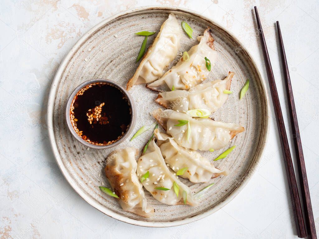 Chinese traditional dumplings - gyoza with pork and vegetables on a round plate with soy sauce in a bowl.