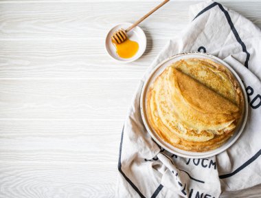 Beyaz tabakta Rus ev yapımı ince krepler ve tahta bal kaşığı ve küçük beyaz tabakta bal. Shrovetide için geleneksel buğday krepleri. Üst Manzara. Boşluğu kopyala
