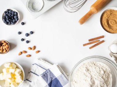 Çeşitli fırın malzemelerinin çerçevesi - un, yumurta, şeker, tereyağı, taze yaban mersini, fındık, mutfak gereçleri ve beyaz arka planda kek pişirme kabı. Üst Manzara. Boşluğu kopyala
