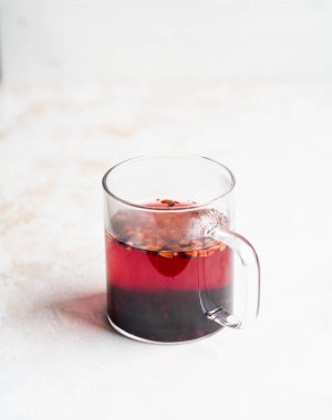 Bir bardak şeffaf kupa, mor sıcak amber çayı ve çeşitli kurutulmuş meyve ve böğürtlen dilimleri.