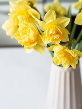 Masadaki vazoda bir buket bahar çiçeği. Vazo yaşam tarzında nergis narsisi.