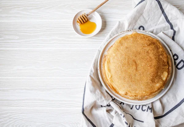 Beyaz tabakta Rus ev yapımı ince krepler ve tahta bal kaşığı ve küçük beyaz tabakta bal. Shrovetide için geleneksel buğday krepleri. Üst görünüm.