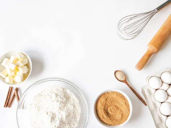 Frame of various baking ingredients - flour, eggs, sugar, butter, dry yeast, nuts and kitchen utensils on white background. Top view. Copy space