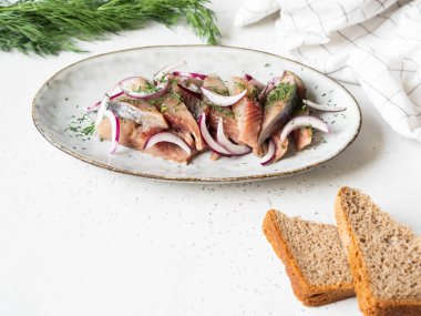 Taze dereotlu ve kırmızı soğanlı marine edilmiş ringa balığı dilimleri, beyaz masada çavdar ekmeği. Boşluğu kopyala