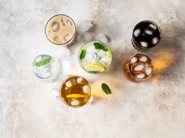 Flat lay of various refreshing drinks in glasses with ice. Apple juice, cola, homemade lemonade, iced coffee, iced tea and sparkling water on beige background. Top view
