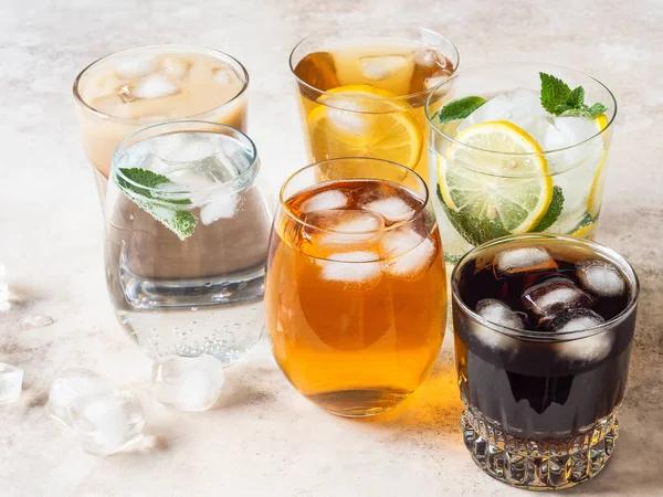 Buzlu bardaklarda çeşitli ferahlatıcı içecekler. Elma suyu, kola, ev yapımı limonata, buzlu kahve, buzlu meyve çayı ve bej arka planda köpüklü su. Boşluğu kopyala