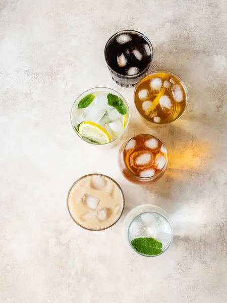 Flat lay of various refreshing drinks in glasses with ice. Apple juice, cola, homemade lemonade, iced coffee, iced tea and sparkling water on beige background. Top view