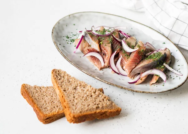 Marinated Herring fish slices with fresh dill and red onion, rye bread on the white table. Copy space