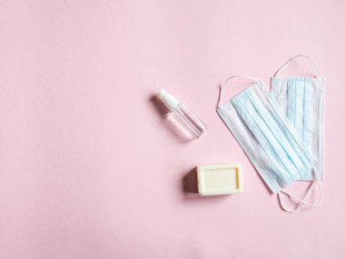 Flat, çeşitli virüslere karşı kişisel koruyucu ekipmanlar kullanıyordu. Tıbbi maskeler, şişe dezenfektanı ve pembe arka planda sabun. Uzayı kopyala Üst görünüm.