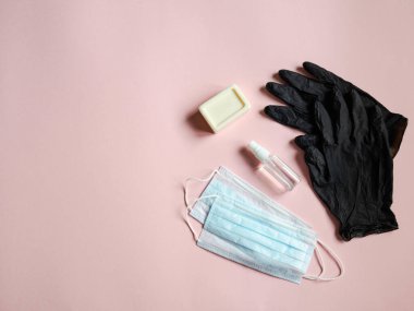 Flat çeşitli virüslere karşı kişisel koruyucu ekipmanlar kullanıyordu - tıbbi maskeler, şişe dezenfektanı, sabun ve pembe arka planda siyah tek kullanımlık eldivenler. Uzayı kopyala Üst görünüm.