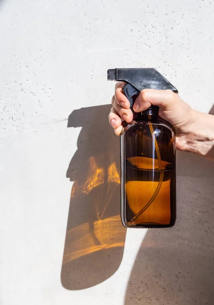 Brown glass spray bottle in female hand sprays liquid on a light background