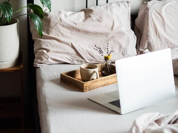 Laptop and coffee on the bed in the bedroom. Work from home or a comfortable pastime online. Stay home, quarantine. Work at home concept.