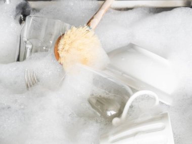 Sabunlu köpük ve odun fırçasında sabunlu suyla birlikte lavaboda çeşitli toprak ve cam eşyalar var.