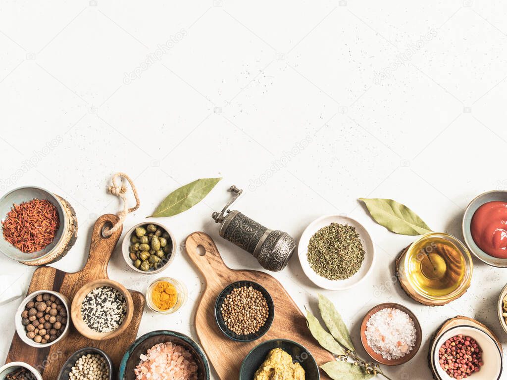A border of various dry spices and sauces on light background. Flat lay of small bowls with dijon mustard, olive oil, ketchup, capers and spices.