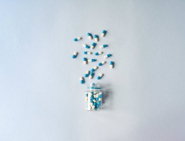 Medical therapeutic dissolving capsules of white and blue colors scattered out of the container on a blue background. Top view. Copy space clipart