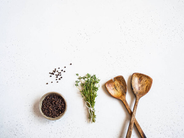 Kitchen composition with wood spoons, black pepper and fresh thyme on light background. Top view. Copy space