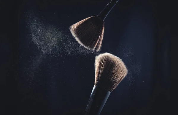 Cosmetic brush with pastel pink cosmetic powder spreading on black background