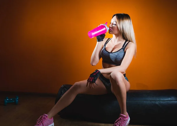 Pretty caucasian fitness girl on diet resting after exercise And drinking protein powder from shaker in the gym — Stock Photo, Image