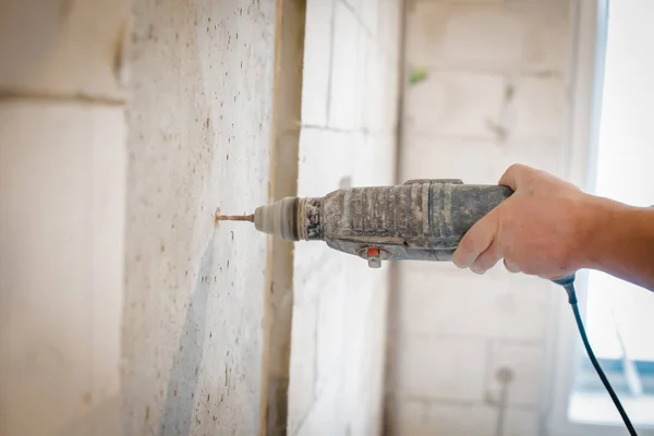 Seorang pria menggunakan bor untuk mengebor dinding. pekerja profesional di lokasi konstruksi — Stok Foto