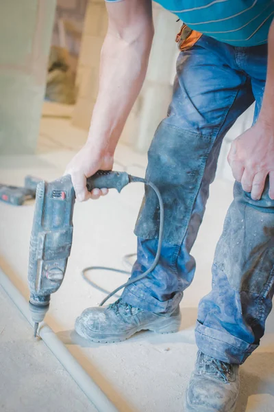 Seorang pekerja menggunakan bor untuk memecahkan permukaan lantai semen — Stok Foto