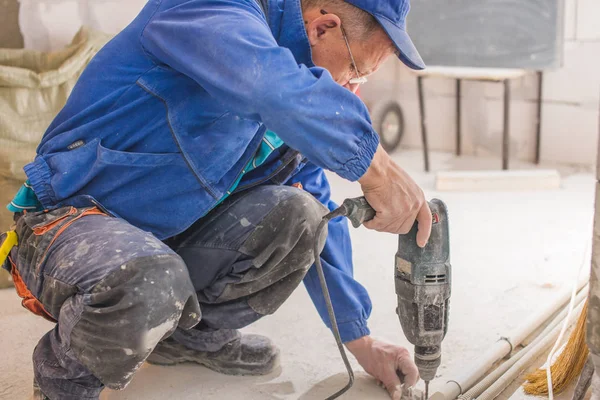 Perbaikan rumah. Tangan laki-laki menggunakan bor perforator listrik dengan bor membuat lubang di dinding dengan cat mengupas . — Stok Foto