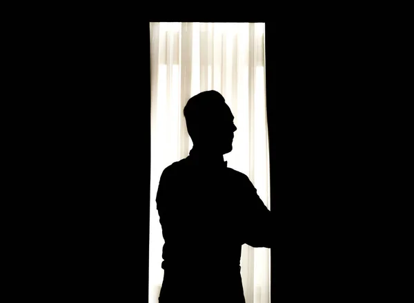 Silhouette of a man standing before a bright window in the dark room — Stock Photo, Image