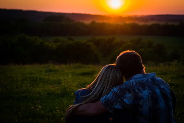 Couple assis dans un champ ouvert, regardant un coucher de soleil, scène romantique. Soleil orange avec brouillard dans les arbres  . — Photo