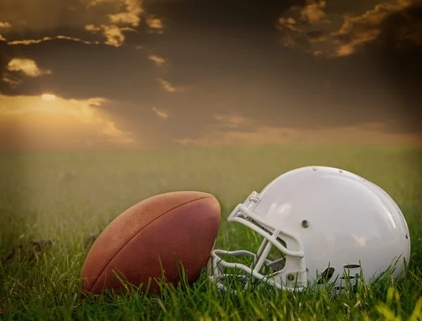 Fútbol americano y casco en el campo al atardecer, con nubes oscuras Fotos de stock libres de derechos