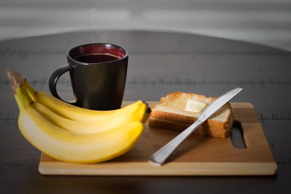 Tostadas con plátanos y taza de café caliente, sobre una mesa redonda de madera oscura. Estilo rústico. Enfoque selectivo con cuchillo mantequilla . Imagen de archivo