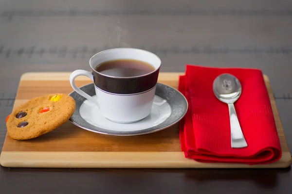 White and black mug of hot strong coffee steam, with chocolate cookies, and a spoon and red napkin on a wooden table — Stock Photo, Image