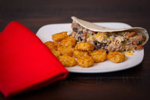 Fajita kip beef burrito's tortilla met rijst en zwarte bonen en tater tots op een ronde houten tafel met een rode servet. — Stockfoto
