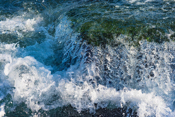 Еще крупным планом изображение проточной воды на темно-зеленых скалах, покрытых мхом
