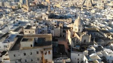 Güneşli bir günde deniz kenarında bir İtalyan şehri. Kilisenin, evlerin ve denizin havadan görünüşü. Monopoli, Puglia, Bari, İtalya 4K