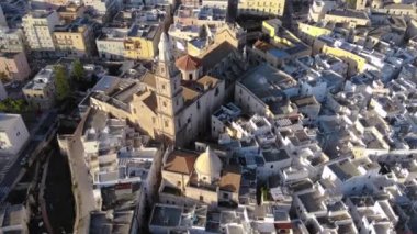 Güneşli bir günde deniz kenarında bir İtalyan şehri. Kilisenin, evlerin ve denizin havadan görünüşü. Monopoli, Puglia, Bari, İtalya 4K