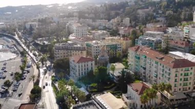 Gün batımında yukarıdan güzel bir İtalyan şehri. Sokaklarda araba trafiği ve palmiye ağaçlarıyla dolu tahta kaldırım. Hava görüntüsü. San Remo, İtalya 4K