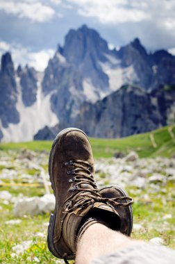 Adam yürüyüşçü bir yere uzanır. Arka plan gibi zirveler. Güneşli bir gün. Trekking botları. Lens parlaması. Başarılı backpacker bir görünüm keyfini çıkarın. 
