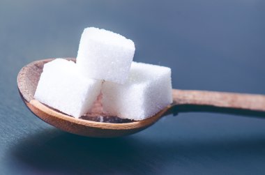 Tahta bir kaşıkta şeker küpleri. Koyu mavi arka plan. Sağlıksız gıda. 