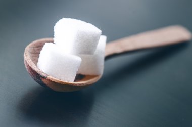 Tahta bir kaşıkta şeker küpleri. Koyu mavi arka plan. Sağlıksız gıda. 