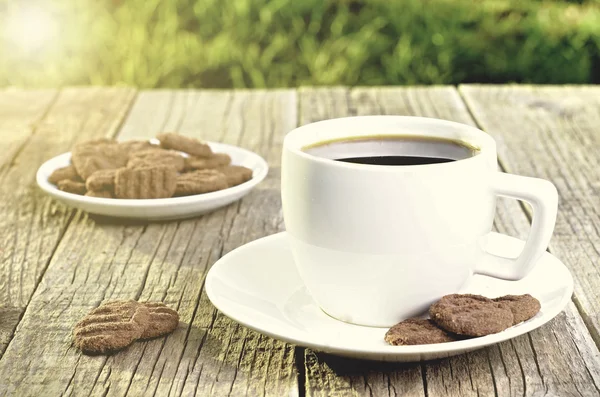 Una taza de café sobre una mesa de madera con galletas. Fondo natural con luces de sol y hierba. Agricultura. Dulce y azúcar . — Foto de Stock